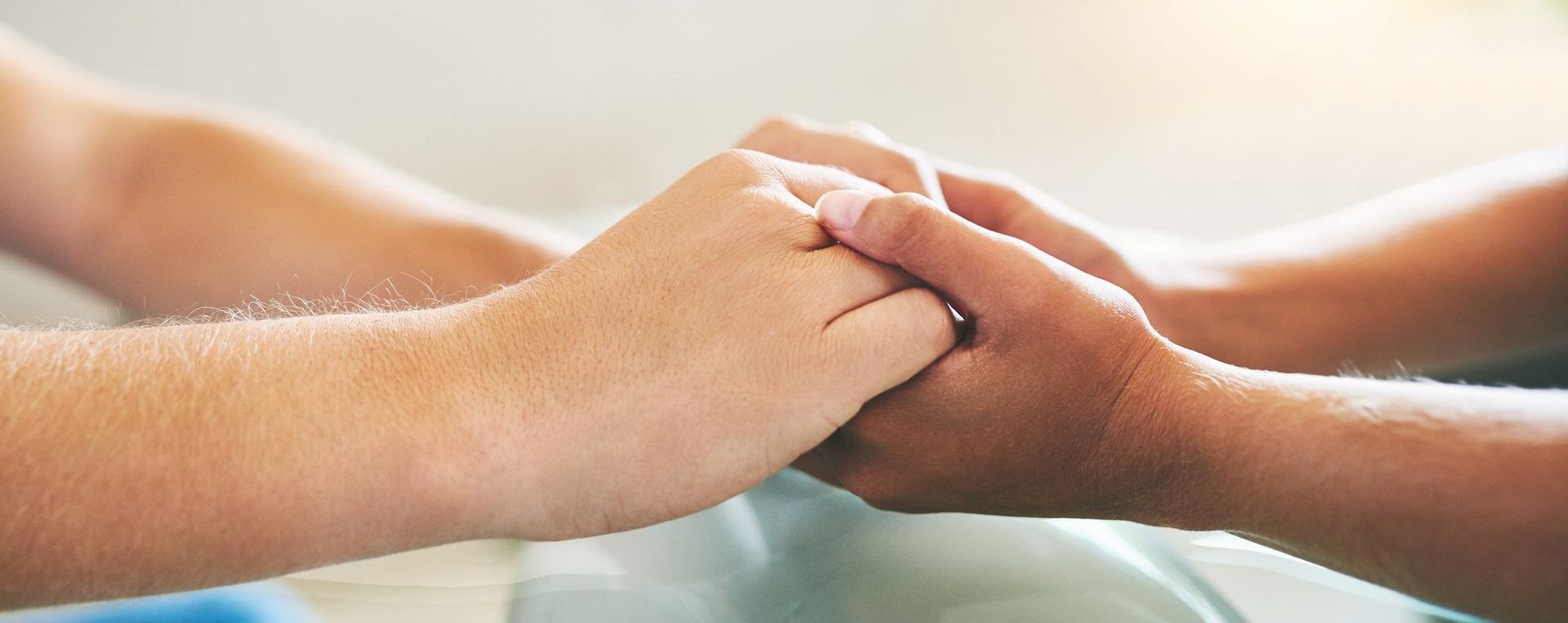 An adult's hand gently cradling a tiny premature baby's hand