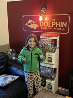A smiling girl in a green jacket beside toy vending machines